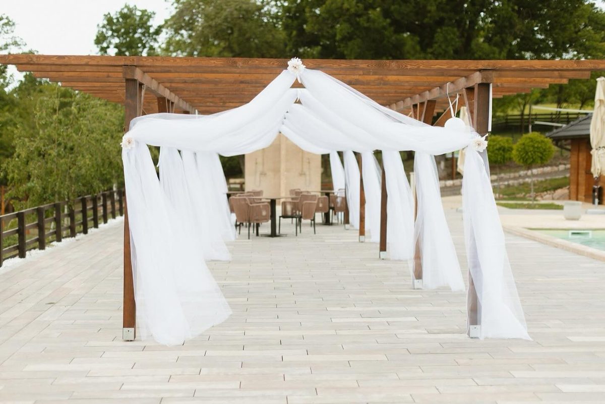 Pergola drapirana belim tilom pored bazena za venčanu ceremoniju