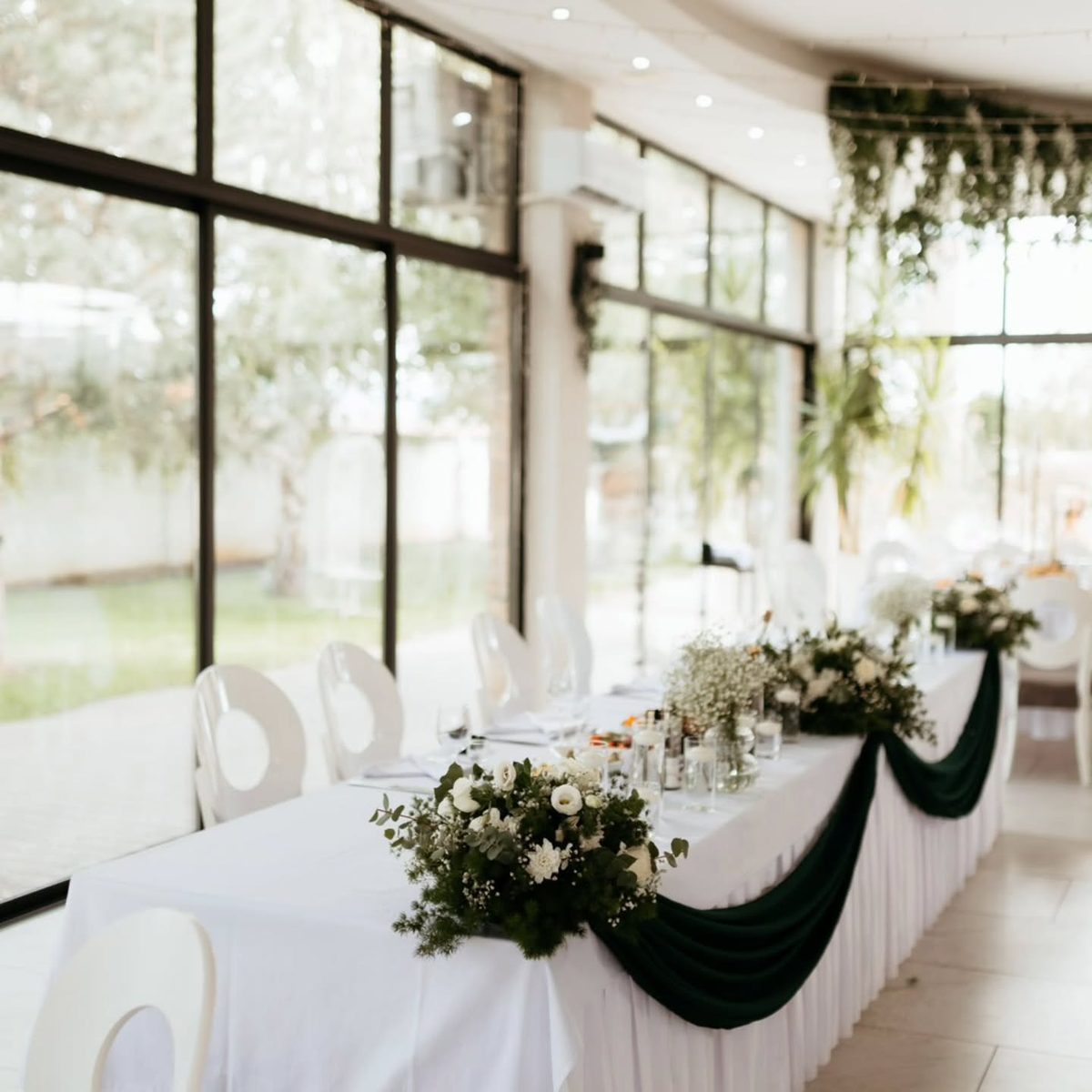 Dekoracija mladenačkog stola sa tamnozelenom draperijom i belim ružama